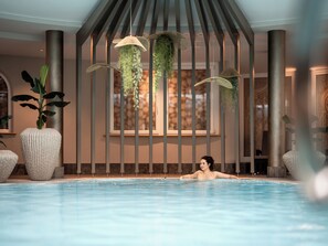 A pool area with a person relaxing, surrounded by large potted plants and hanging planters.