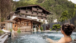 A wooden cabin with a hot tub in front, surrounded by a forested mountain backdrop. - Hotel Rita (Laengenfeld)