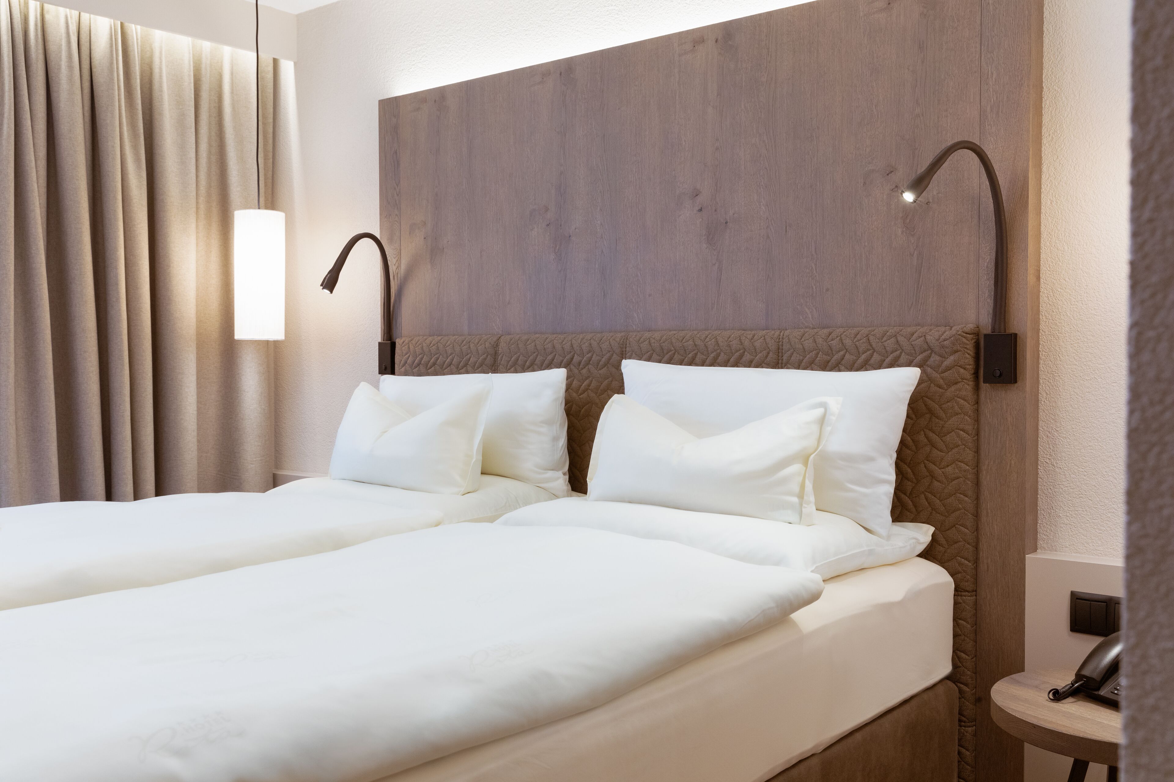 A hotel room with a double bed, two bedside lamps, a wooden headboard, and a bedside telephone.