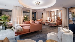 A modern living room with a large, round ceiling light, plush seating, and a view into the adjacent room. - Hotel Rita (Laengenfeld)