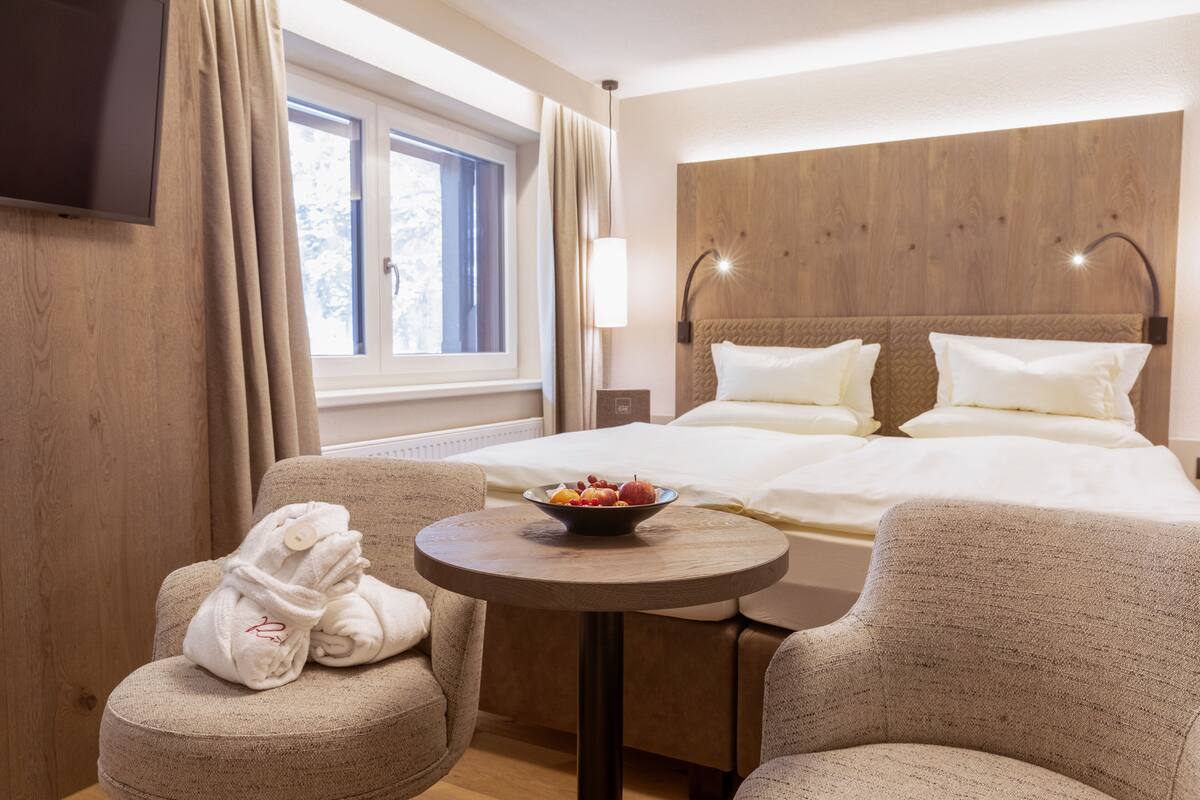 A hotel room with a bed, a small round table with a bowl of fruit, and two armchairs.