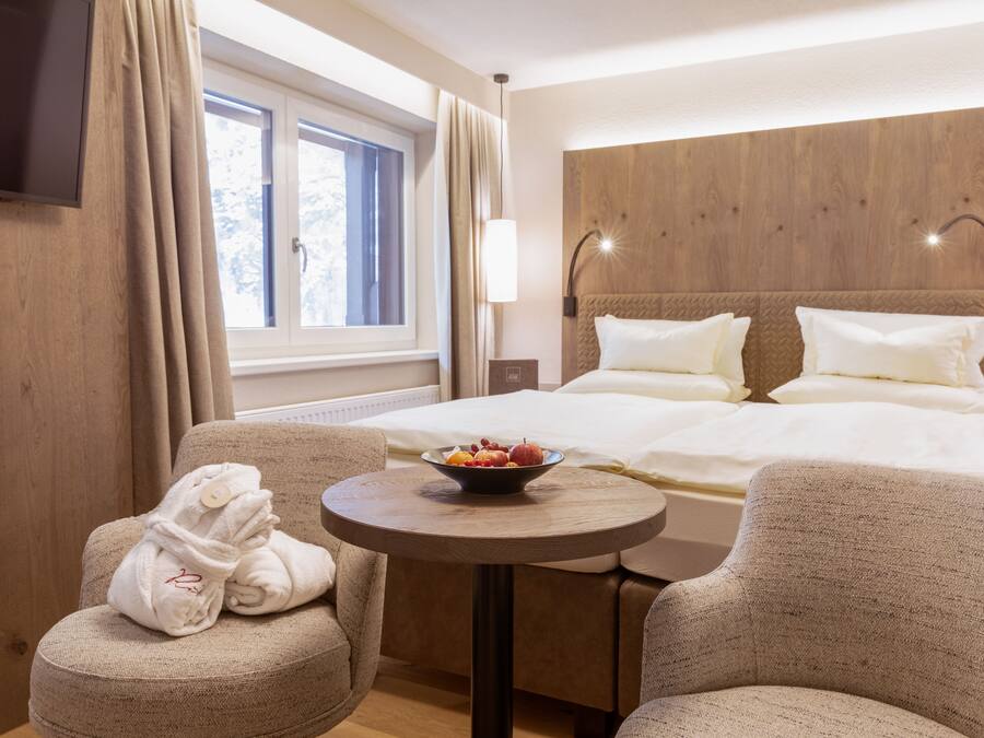 A hotel room with a bed, a small round table with a bowl of fruit, and two armchairs.
