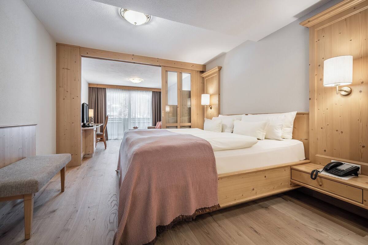 A hotel room with a bed, bedside table, desk, chair, and a view of the outside.