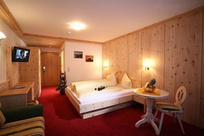 Een hotelkamer met een houten paneelwand, een bed met wit beddengoed, een klein rond tafeltje met een stoel, en een aan de muur bevestigde televisie.