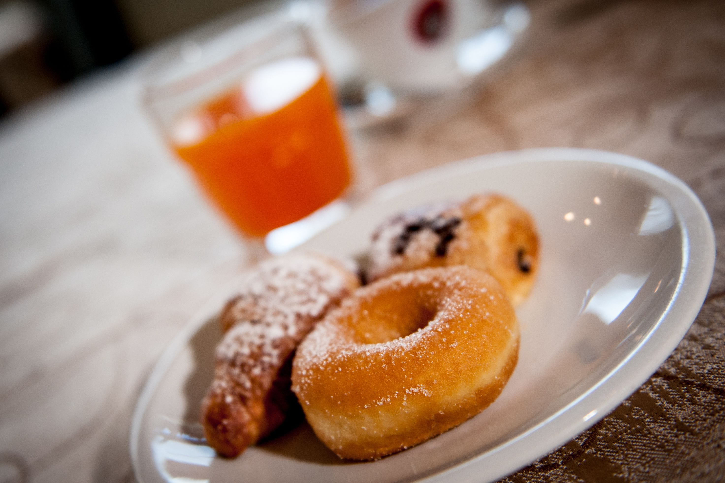 A plate of doughnuts with powdered sugar and a glass of orange juice on a table.