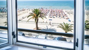 A beach view from a window with a clear sky, palm trees, and beach umbrellas. - Hotel Villa Eleonora (Minturno)