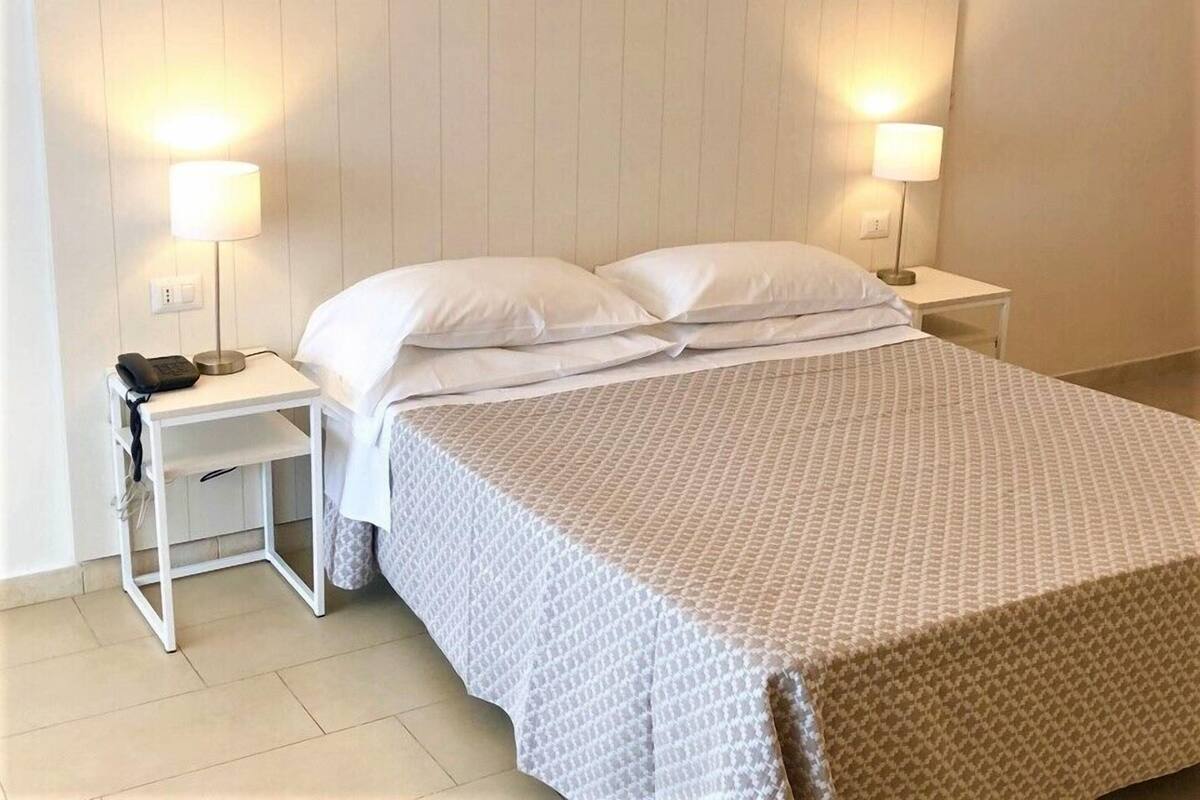 A neatly made bed with white bedding, two bedside lamps, and a small bedside table with a phone.