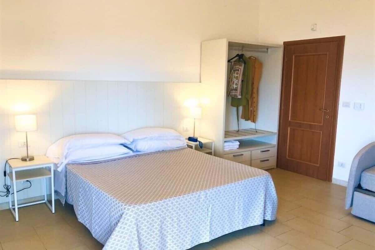 A neatly arranged bedroom with a bed, bedside lamps, a wardrobe, and a door.