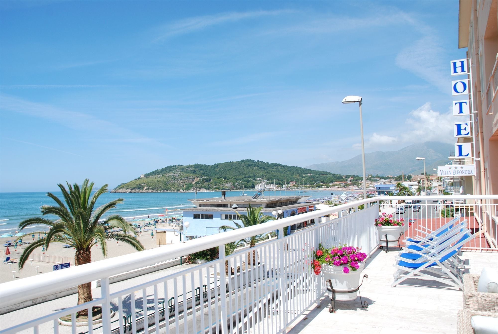 A hotel balcony with a view of the beach, a mountain, and a clear sky.
