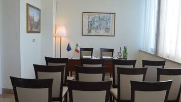 A conference room with a table, chairs, flags, a lamp, and a painting on the wall.