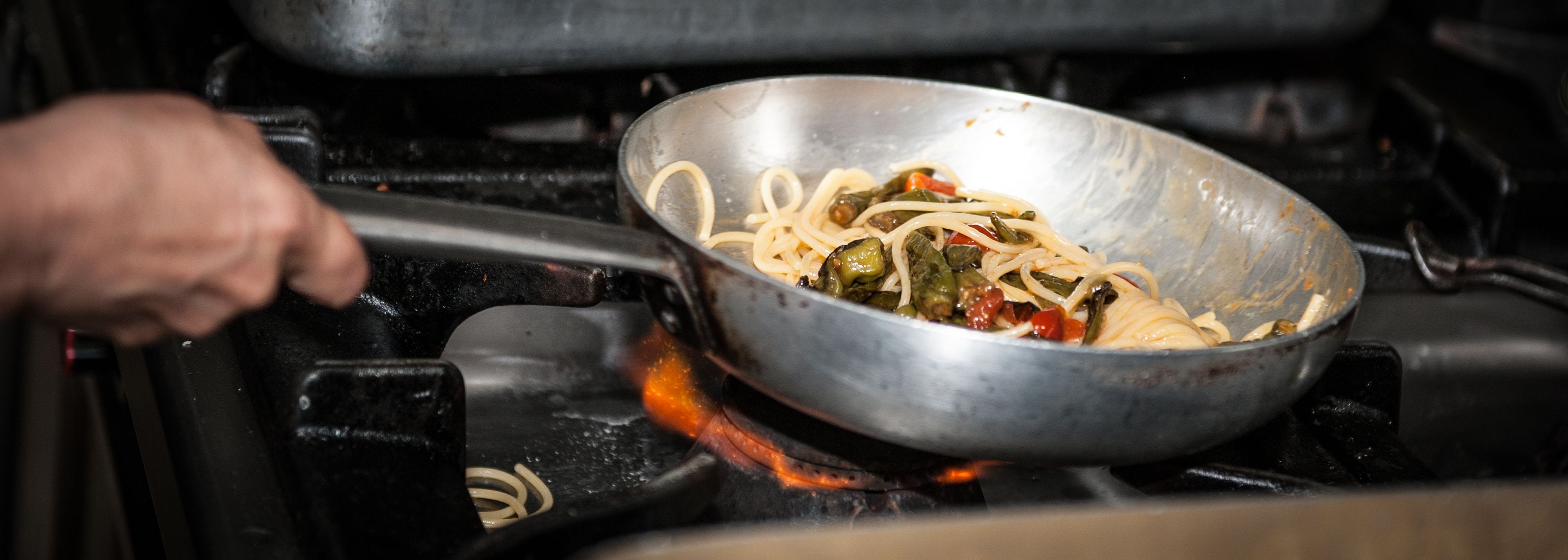 A wok on a stove with noodles and vegetables being cooked.