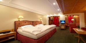 A hotel room with a large bed, a desk with a television, and a seating area with a red curtain backdrop.