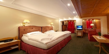 A hotel room with a large bed, a desk with a television, and a seating area with a red curtain backdrop.