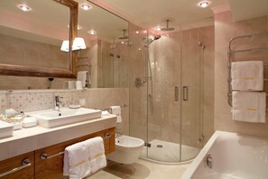 A modern bathroom with a glass-enclosed shower, a freestanding bathtub, and a vanity with a mirror. - Sporthotel Lorv Nser (Lech am Arlberg)
