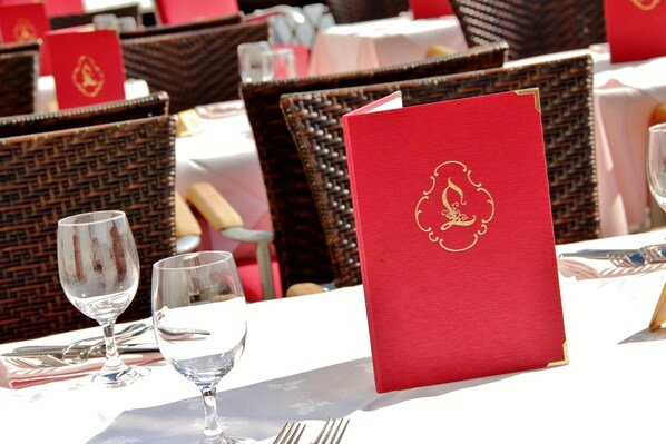 Une table dressée avec un menu rouge, deux verres à vin et des couverts.