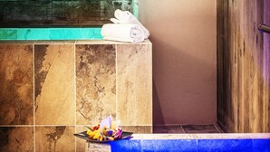 Un área de spa con una pared de piedra, un cartel que dice "POZZO CHIACCATO MIKEVEH FROZEN POOL MIKEVEH", un perchero y un cuenco pequeño con flores.