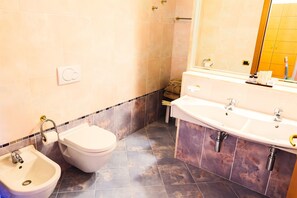 Un baño con inodoro, bidé y un lavamanos grande con espejo superior.