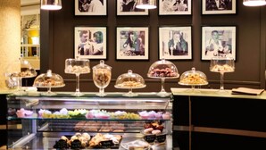 Una vitrina de pastelería con diversos pasteles y postres bajo campanas de cristal, y una pared con fotografías enmarcadas.