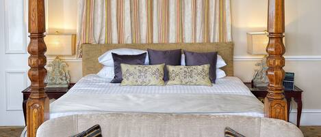 A four-poster canopy bed with a checkered bedspread and multiple pillows, a tufted sofa with striped cushions, and a patterned carpet.