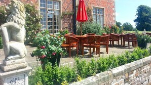 Un patio con una estatua de león de piedra, sillas de madera y un paraguas rojo.