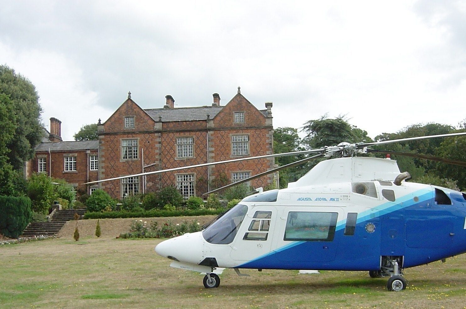 A helicopter parked in front of a large, historic brick building with multiple windows and a staircase leading to the entrance.
