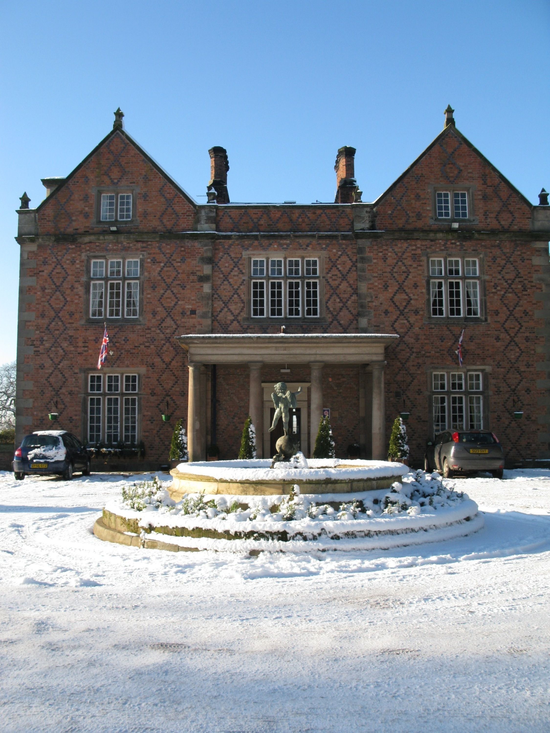 A large brick building with a symmetrical facade, a central entrance with columns, and a statue in front.