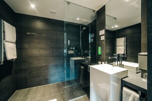 A modern bathroom with dark tiles, a glass shower enclosure, and two white sinks.