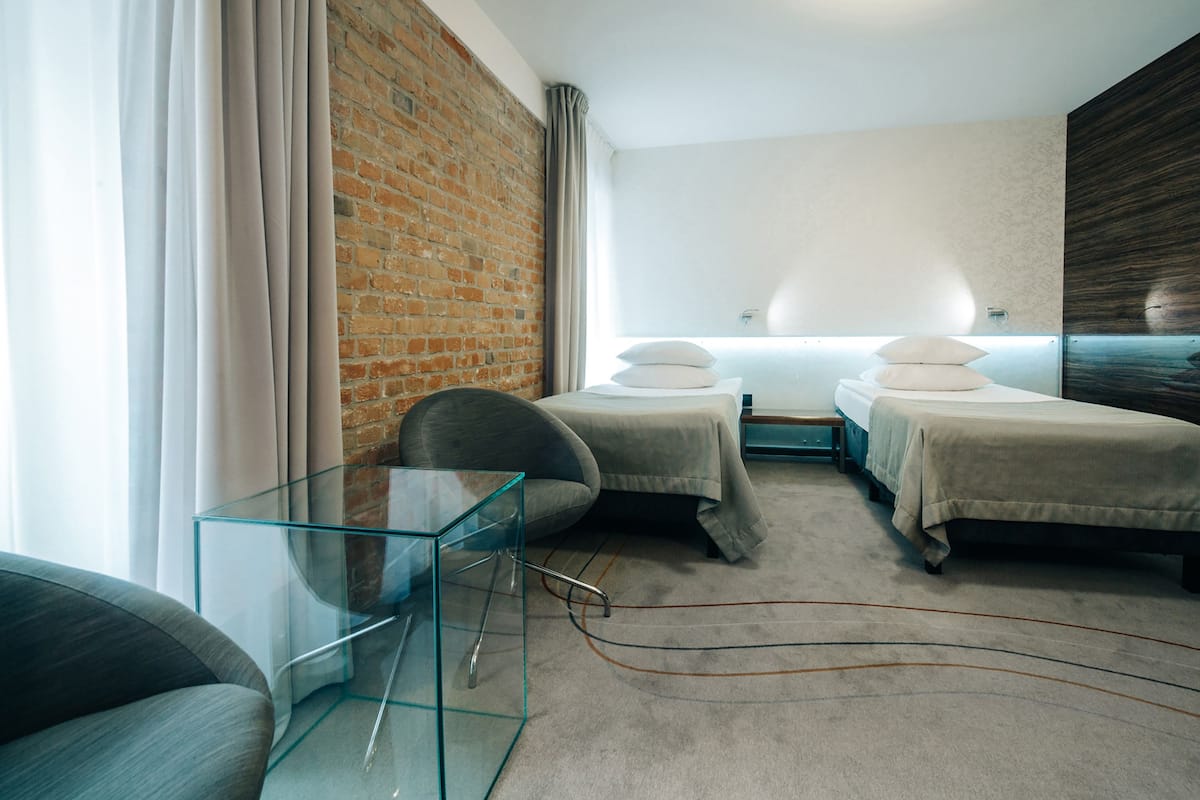 Habitació d'hotel moderna amb dos llits, una taula de vidre i una paret de maó.