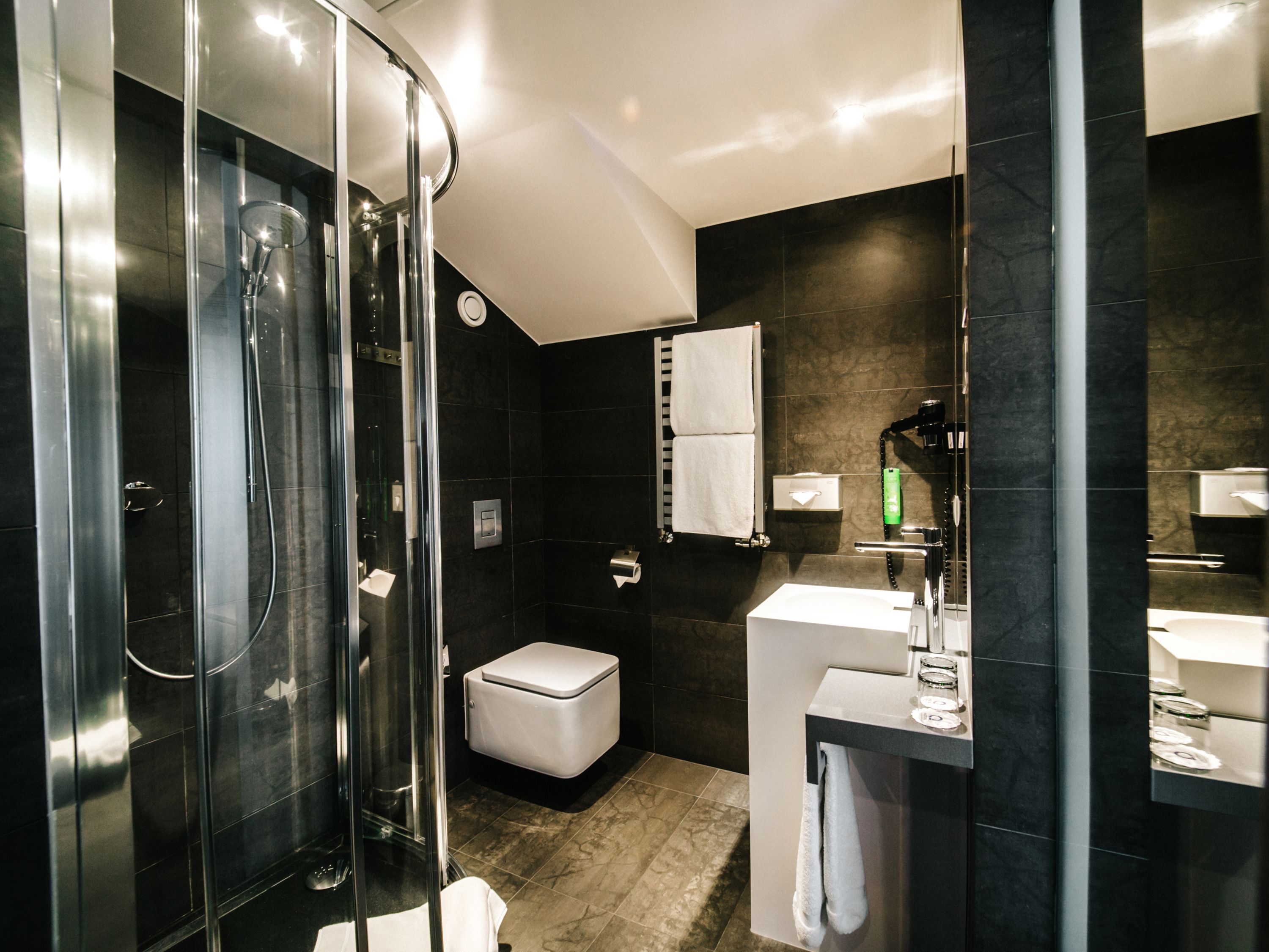 Ein modernes Badezimmer mit Duschkabine aus Glas, einer weißen Toilette, einem Waschbecken mit Spiegel und einem Handtuchhalter.