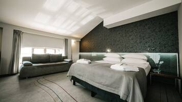 Ein modernes Hotelzimmer mit einem großen Bett, einer Couch, einem großen Fenster mit Vorhängen und einer Wand mit dunklem Muster.