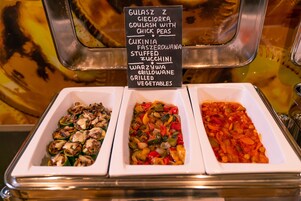 Un buffet proposant une variété de plats, chacun étant clairement identifié, notamment des courgettes farcies, des légumes grillés et du poulet aux pois chiches.