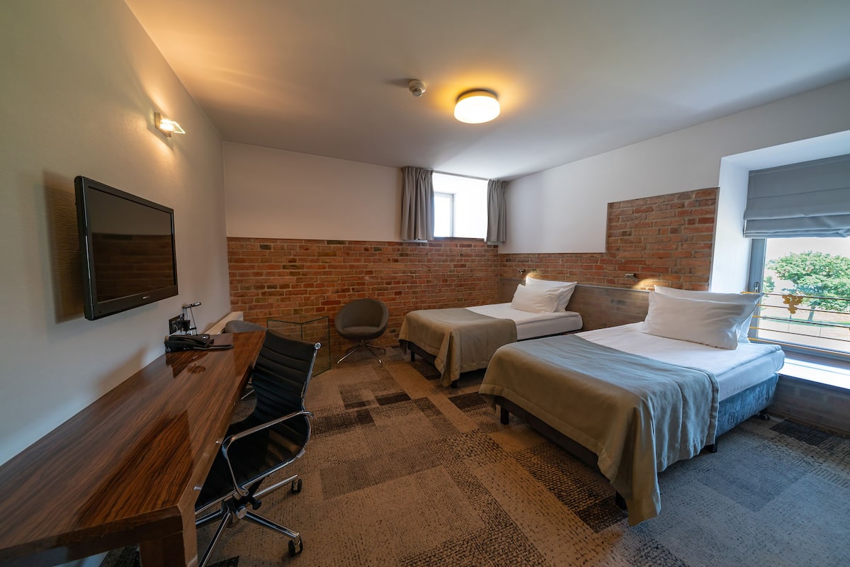 Habitació d'hotel amb escriptori de fusta, dos llits, televisió i paret de maó.