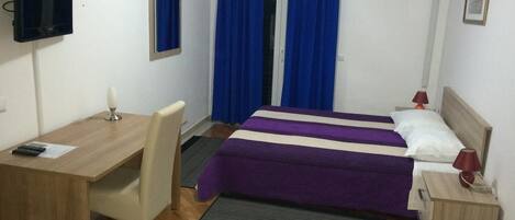Una camera d'albergo con un letto, una scrivania, una sedia, una televisione e tende.