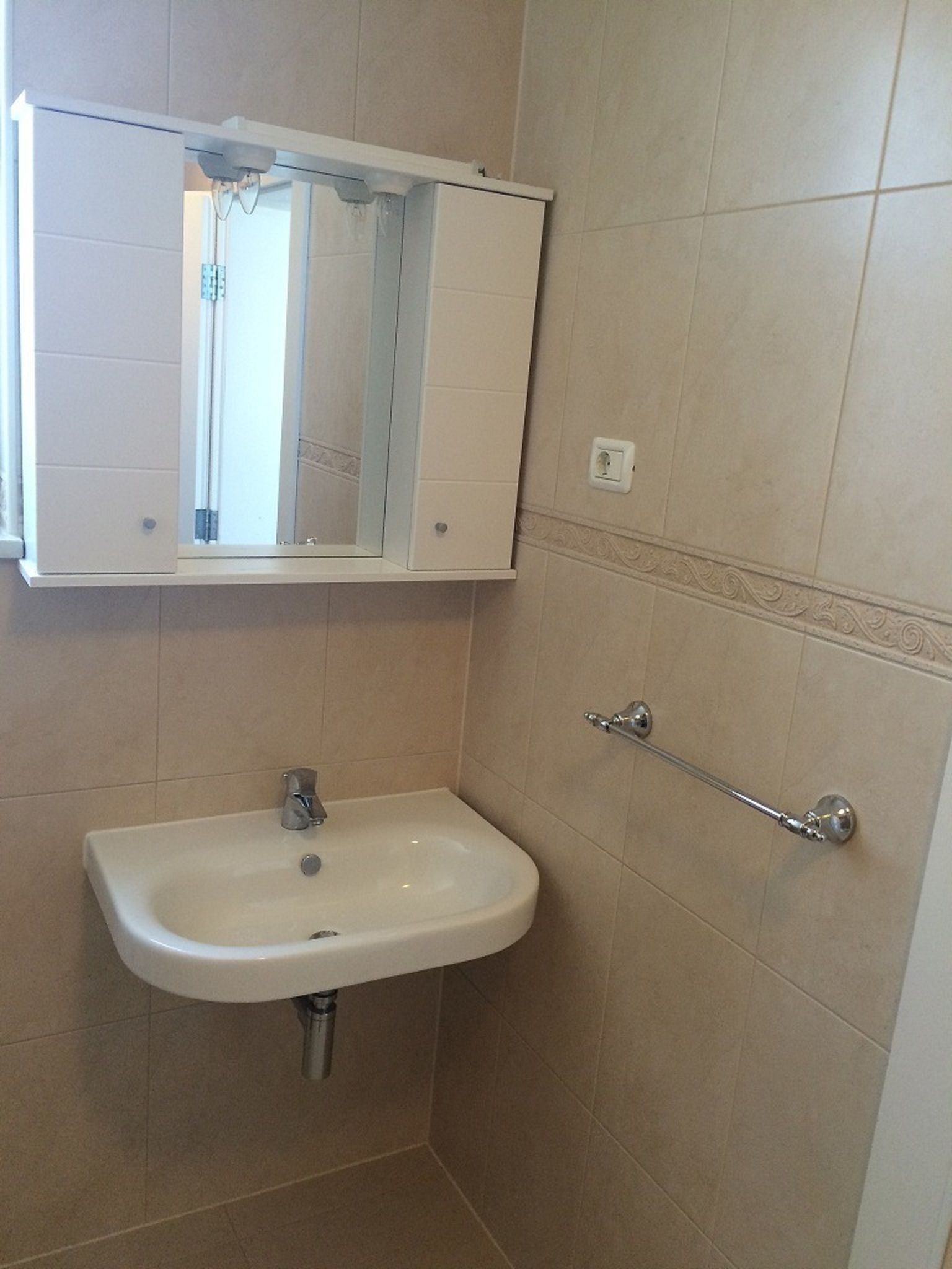 Ein Badezimmer mit einem weißen Waschbecken, einem Spiegel darüber und einem Handtuchhalter an der Wand.
