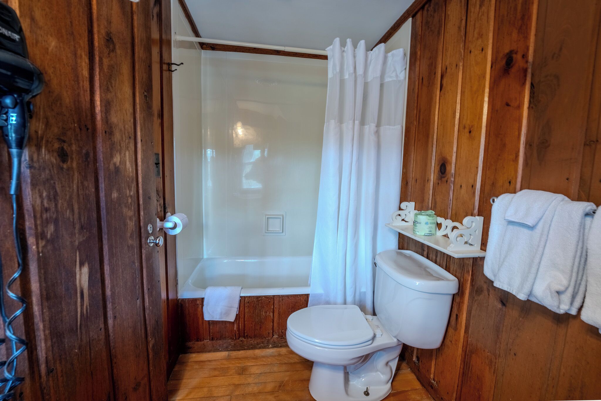 A wooden bathroom with a bathtub, toilet, and shower curtain.