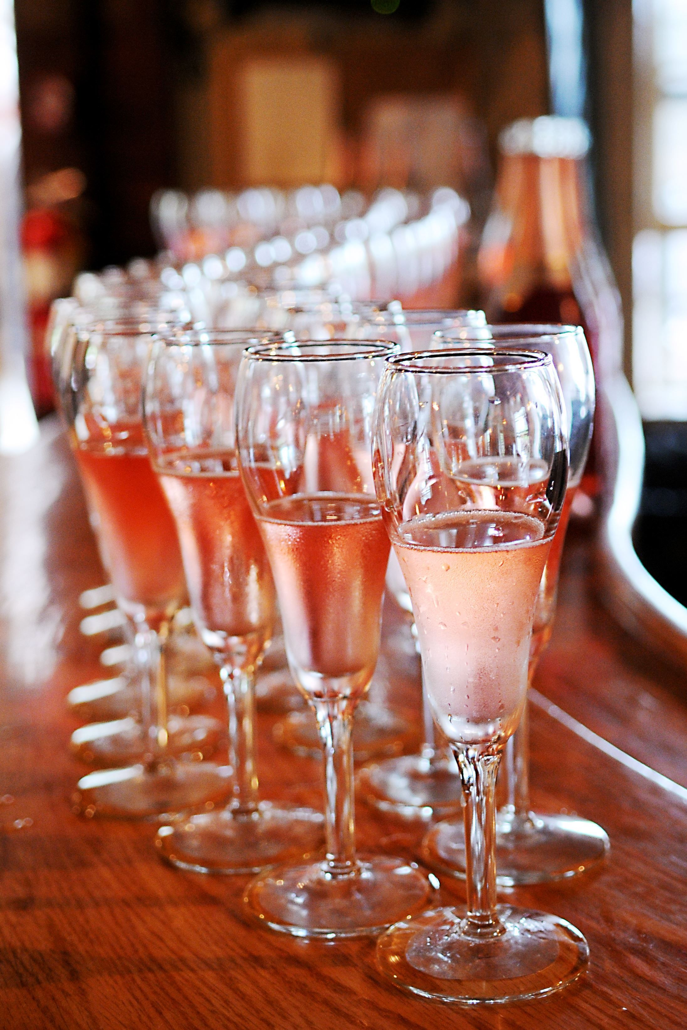 A row of champagne flutes on a wooden bar counter.