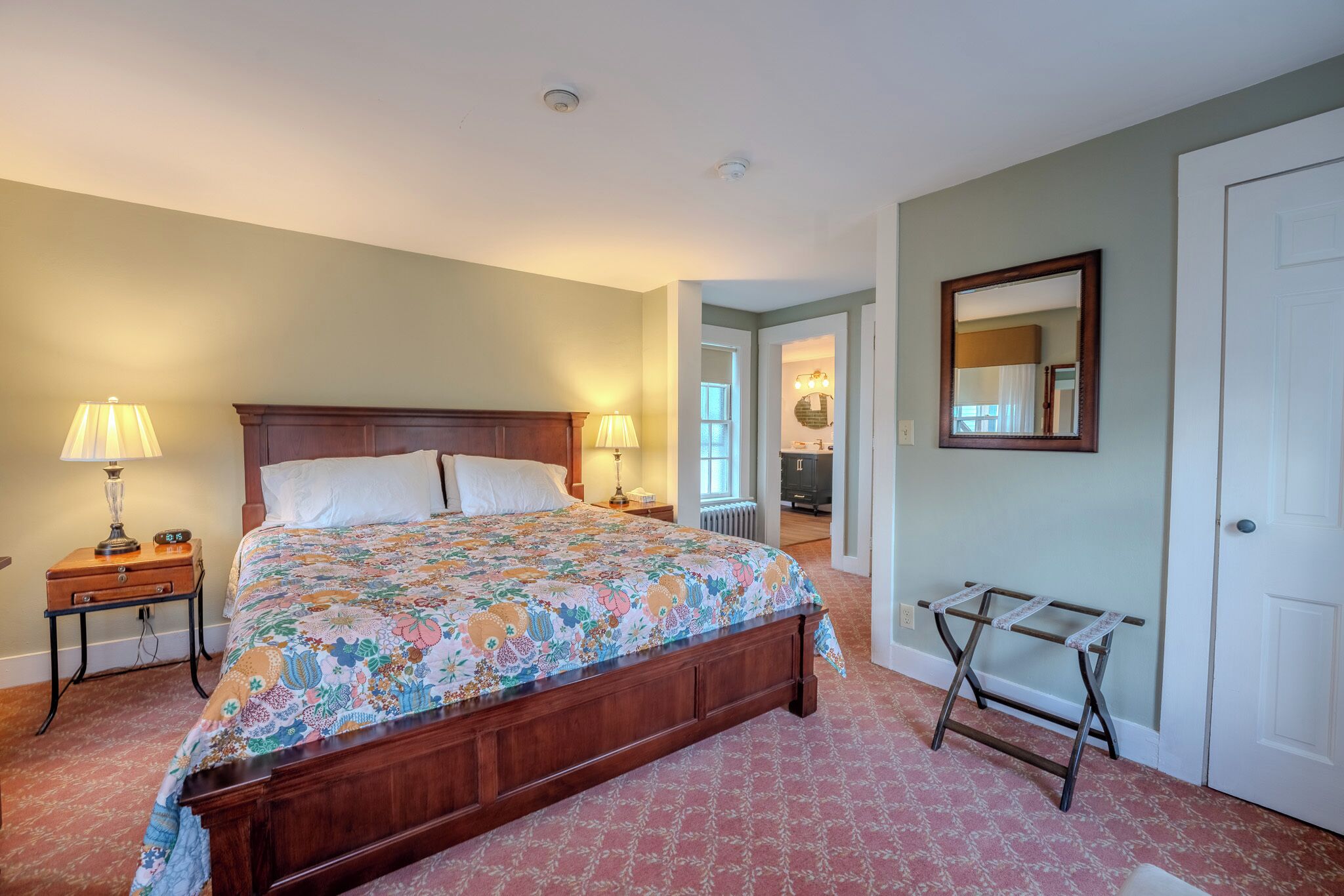 Une chambre à coucher avec un lit en bois, deux tables de chevet avec des lampes, un radiateur, un miroir et une porte.