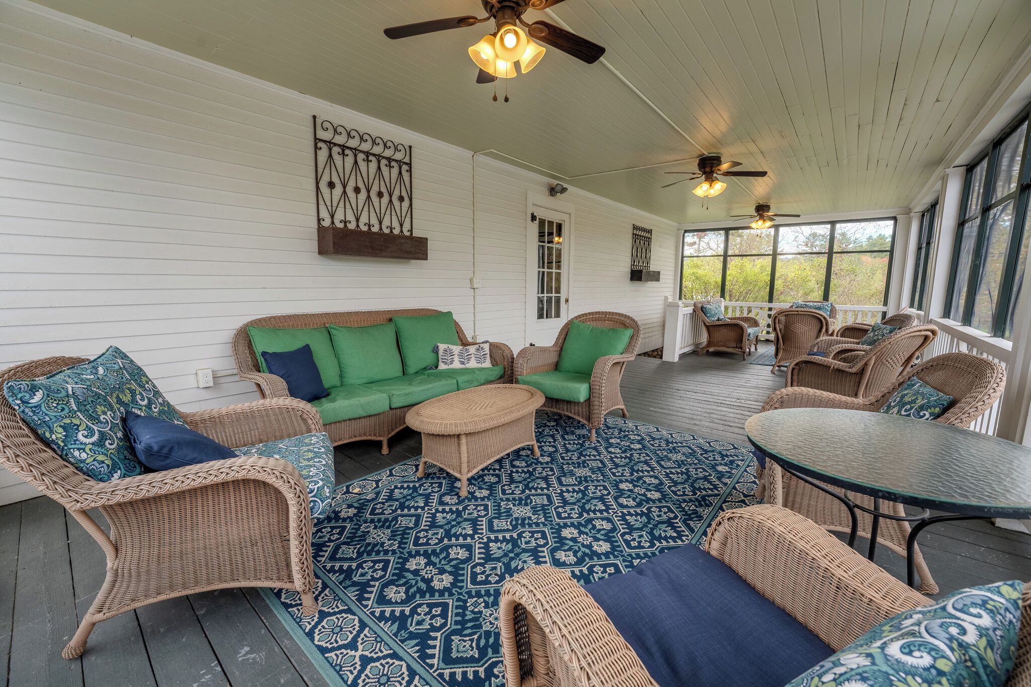 A covered porch with wicker furniture, a patterned rug, and ceiling fans.