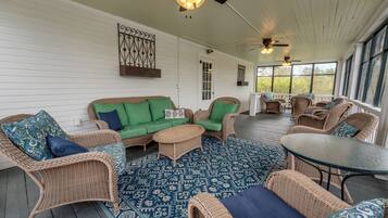 A covered porch with wicker furniture, a patterned rug, and ceiling fans.