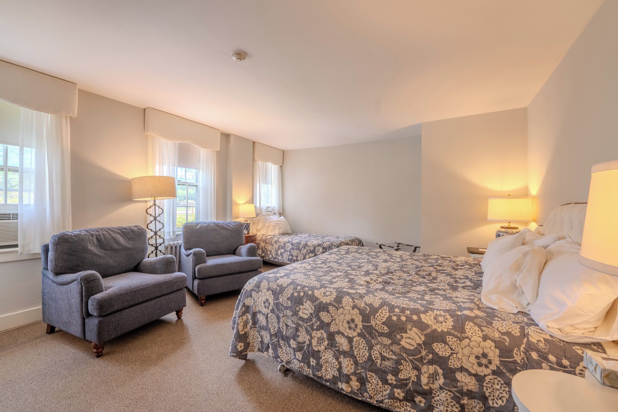 A hotel room with a large bed, two armchairs, a small table, and a lamp.