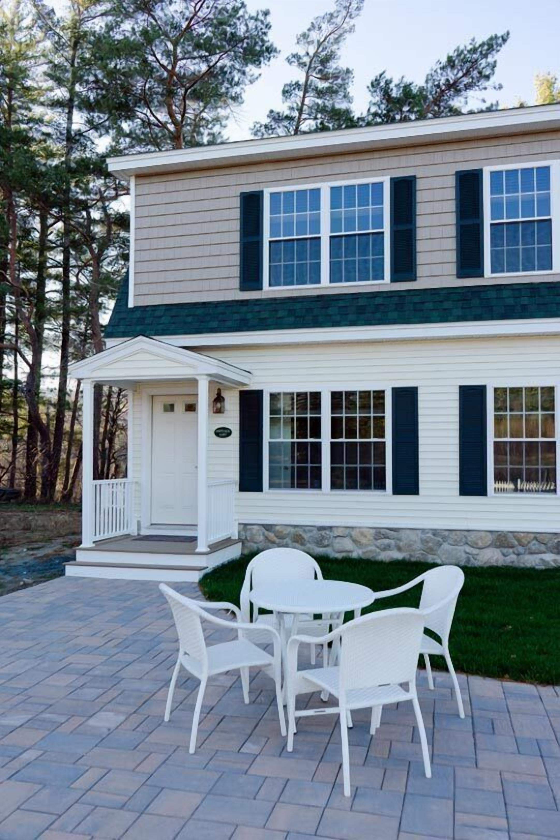 A two-story house with a porch and a patio with white chairs.