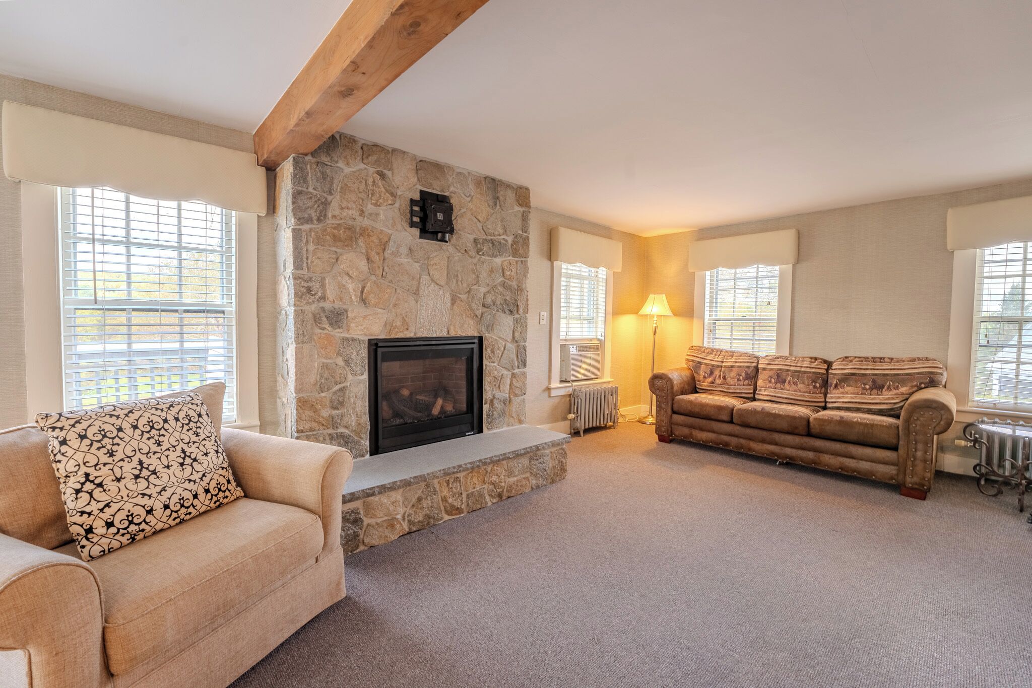 A living room with a stone fireplace, beige sofa, and a brown leather couch.