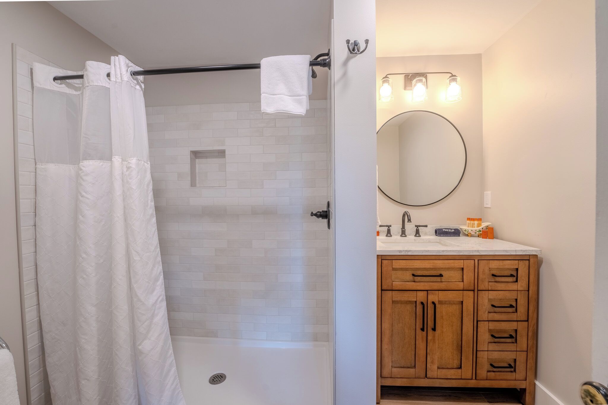 A bathroom with a shower, a toilet, a sink with a mirror, and wooden cabinets.
