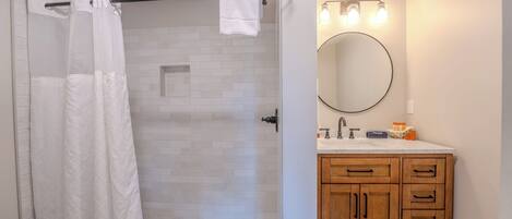 A bathroom with a shower, a toilet, a sink with a mirror, and wooden cabinets.