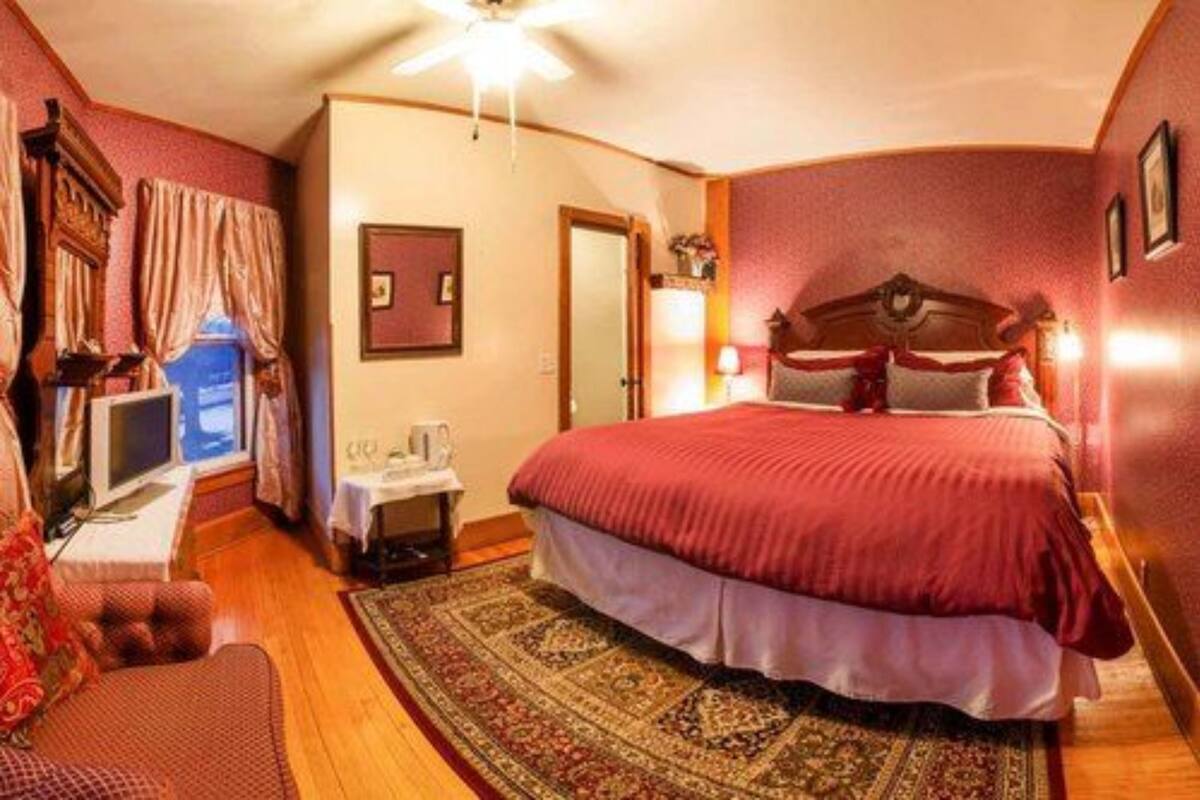Une chambre à coucher avec un grand lit, un bureau avec un ordinateur, une chaise et une fenêtre avec des rideaux.