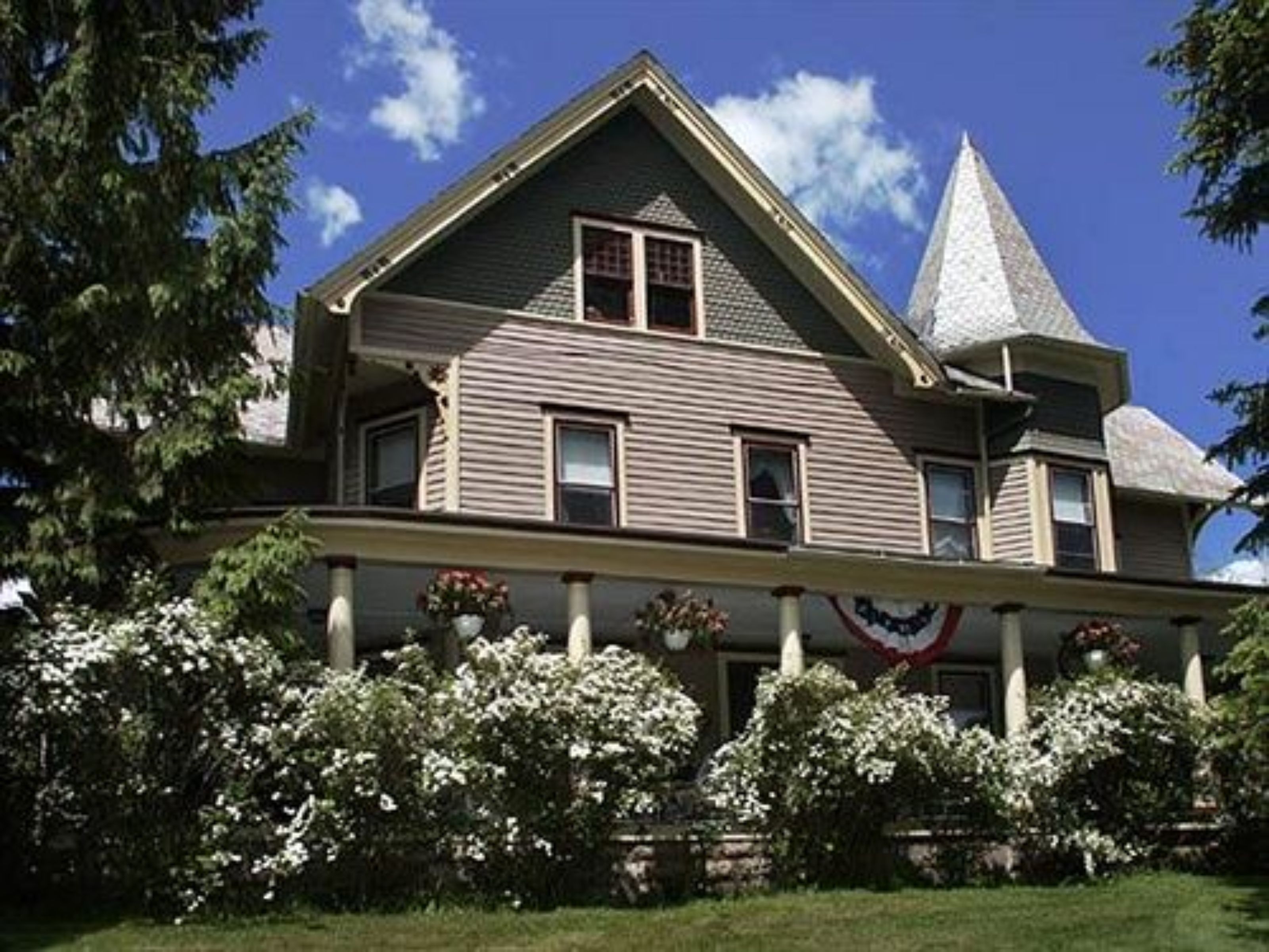 Une grande maison à deux étages, dotée d’un toit à forte pente et d’une structure imposante en forme de tour sur le côté droit.