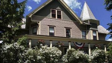Une grande maison à deux étages, dotée d’un toit à forte pente et d’une structure imposante en forme de tour sur le côté droit.
