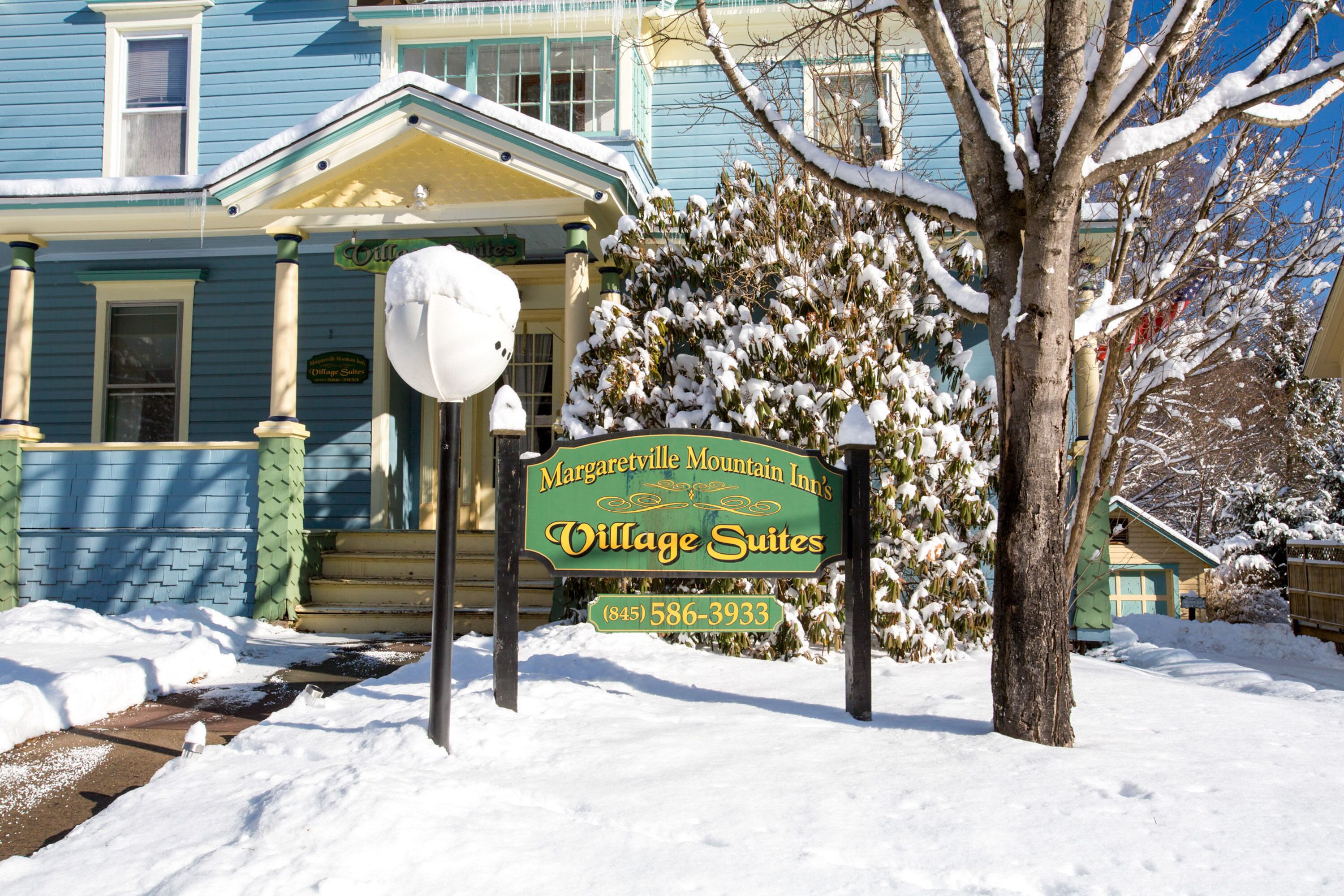 Esterno innevato delle Village Suites del Margaretville Mountain Inn, con un cartello verde che mostra il nome e il numero di telefono.