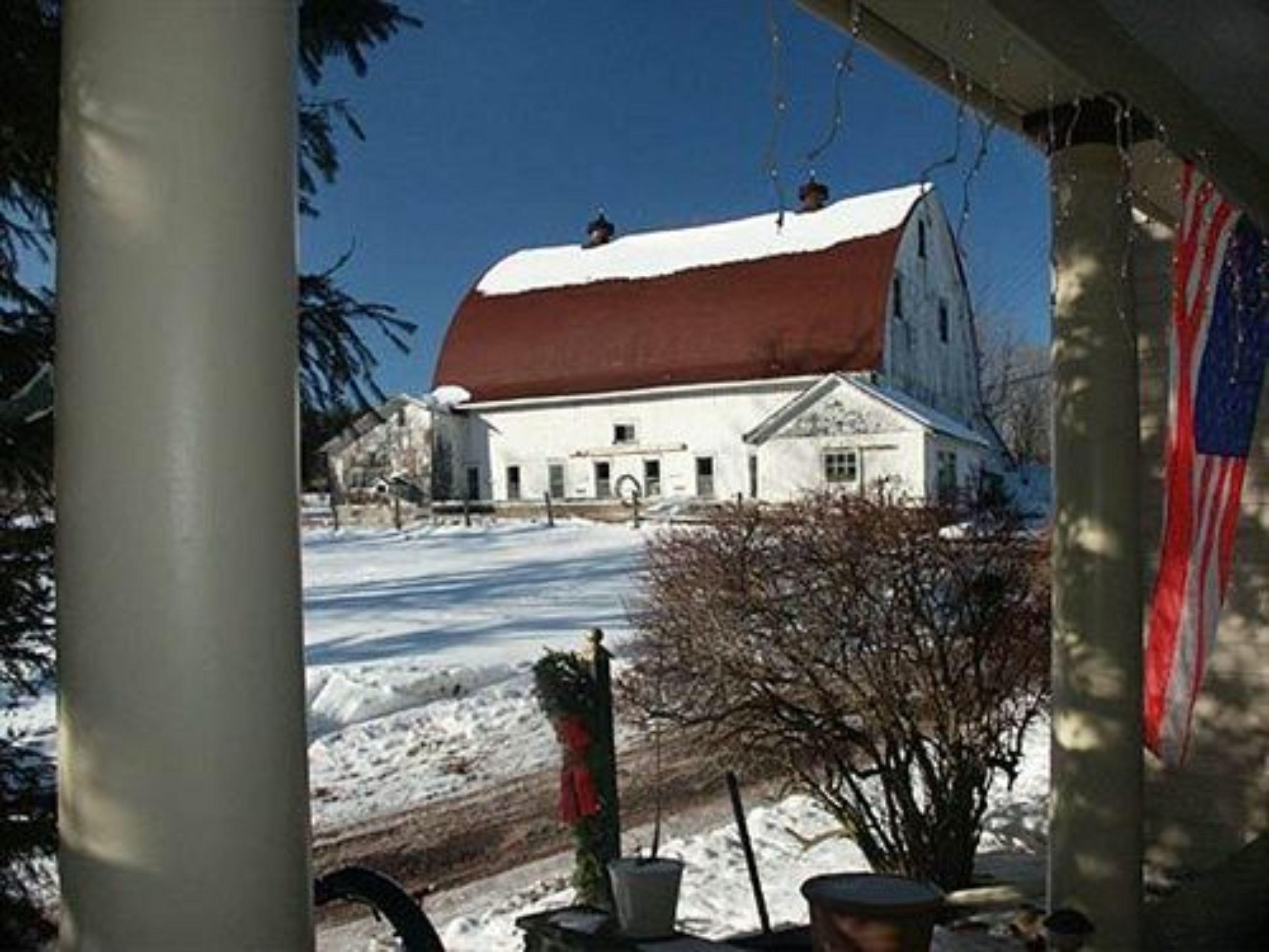 Um edifício branco com telhado vermelho, rodeado por neve, e uma bandeira americana visível.