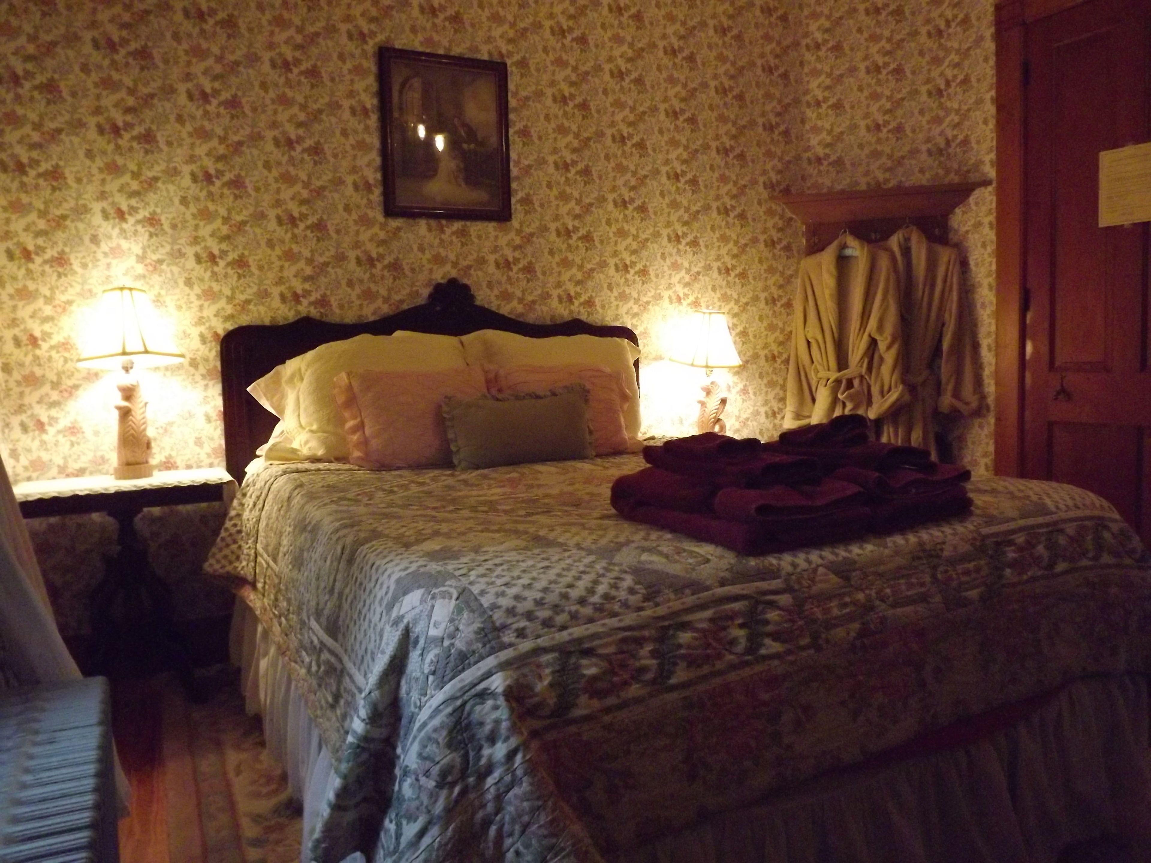 A bedroom with a floral wallpaper, a wooden headboard, two bedside lamps, and a bed with a patterned bedspread and pillows.